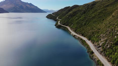 aerial pull back of scenic winding road reveal lake surrounded by mountains