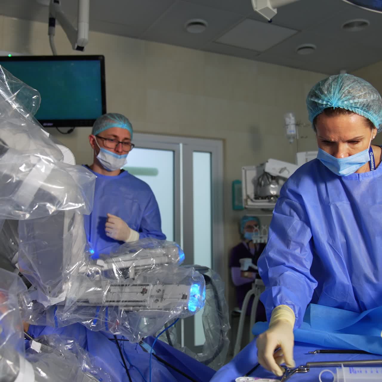 Assistant closes the container and rises a sheet on the tool table. Nurse chooses the necessary instruments for operation. Robot Da Vinci is in the room beside