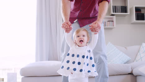 Father-helping-daughter-learn-to-walk-at-home,-front-view