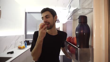 Healthy-eating,-food-and-diet-concept---happy-young-man-seeking-for-food-in-fridge,-taking-apple-from-fridge-at-home-kitchen-and-close-it.-Footage-from-inside