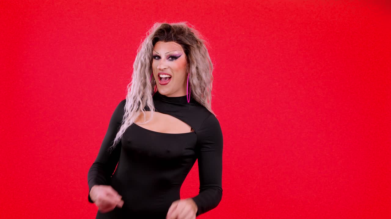 Drag queen in posa e che indica su sfondo rosso