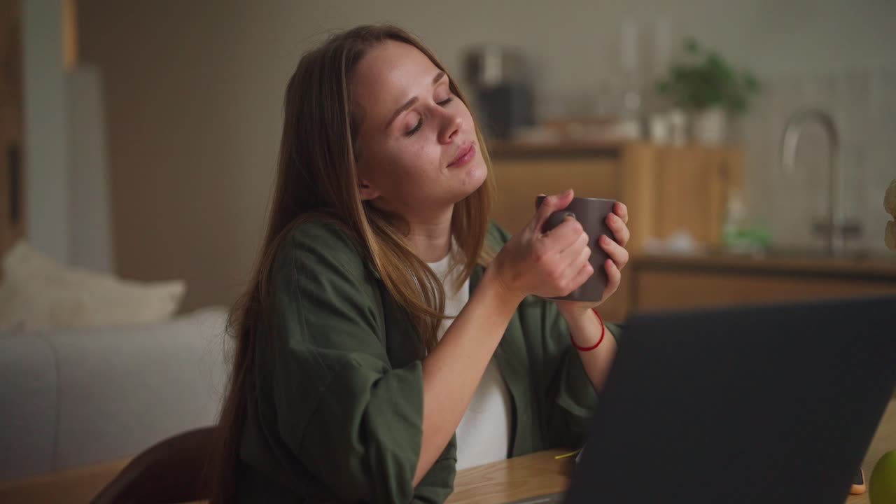 mujer disfrutando de una bebida caliente en casa mientras trabaja en su portátil