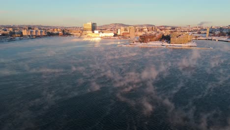 Vista-De-La-Hora-Dorada-Sobre-Bjorvika-En-El-Distrito-Sentrum-De-Oslo,-Noruega,-Con-Niebla-Flotando-Sobre-El-Agua