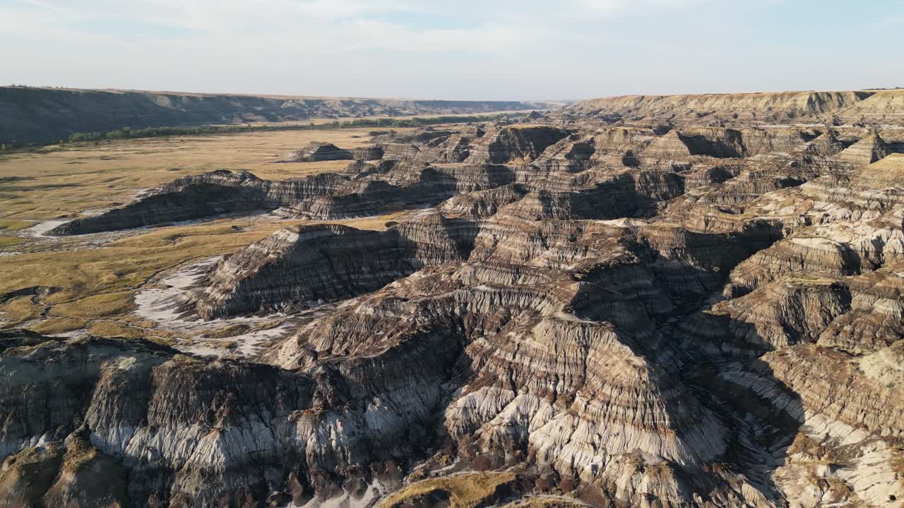 Aerial view of large eroded badlands hills in Alberta, Canada, filmed by drone shortly before sunset with warm evening light and rugged terrain visible