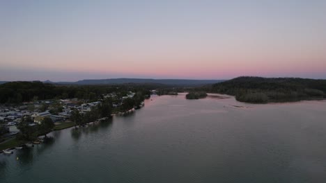 Aerial-holiday-town-on-river-at-sunrise-pink-sky-Lake-Conjola,-Australia