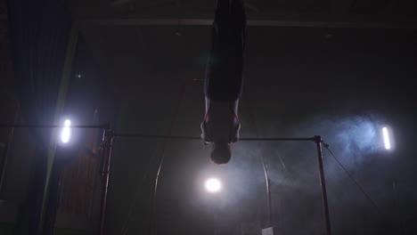 Gymnast-on-a-dark-background-on-the-crossbar-performs-spins-and-jumps-over-himself-in-the-air-in-slow-motion-and-around-the-smoke