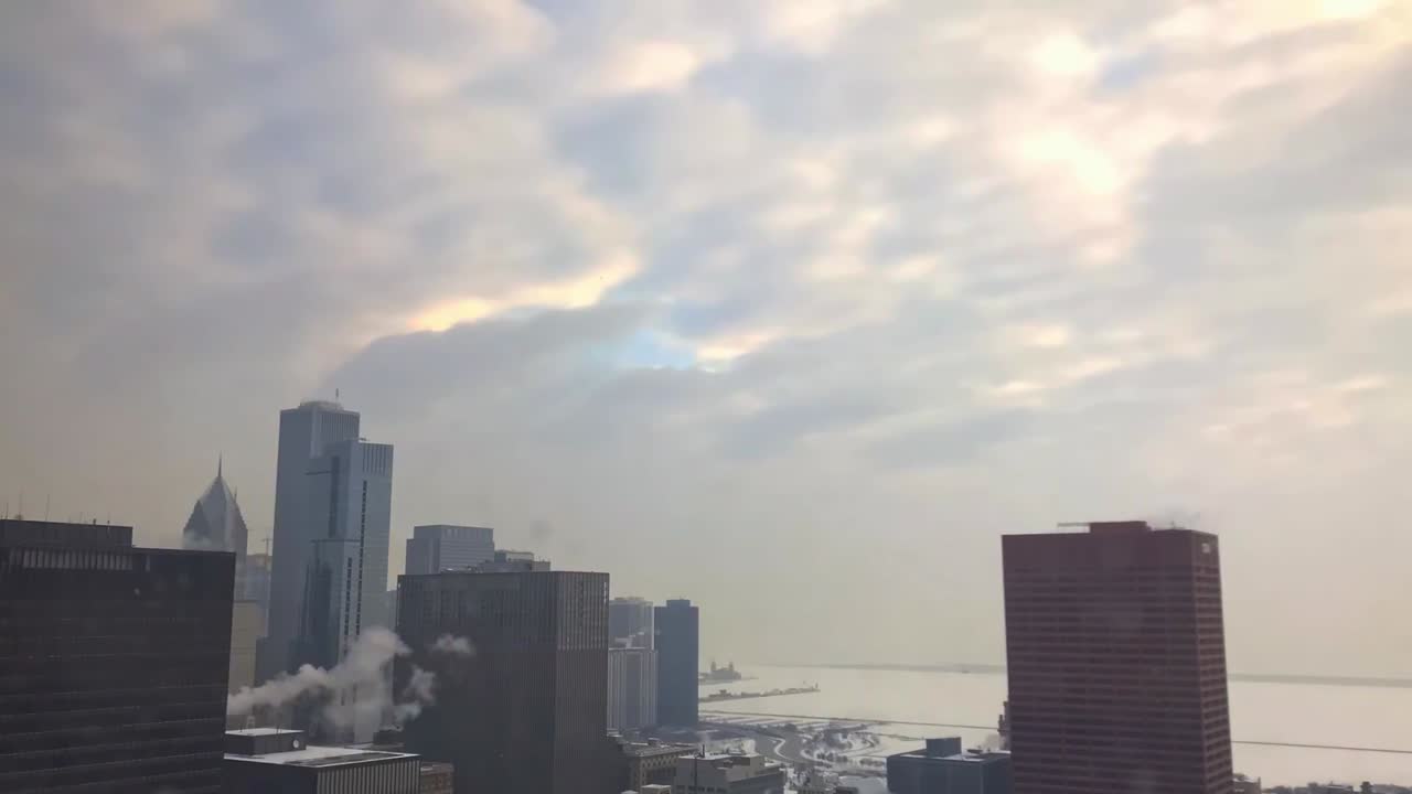Lapso de tempo do horizonte nebuloso de inverno de Chicago com sol baixo atrás das nuvens e vapor subindo dos edifícios.