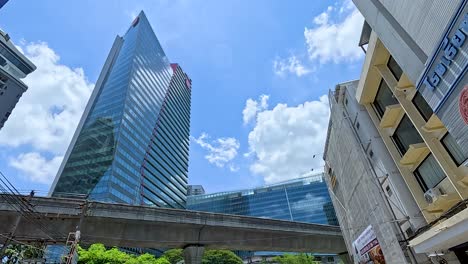 high-rise buildings under a bright blue sky in bangkok. street activity includes pedestrians and vehicles, capturing urban life