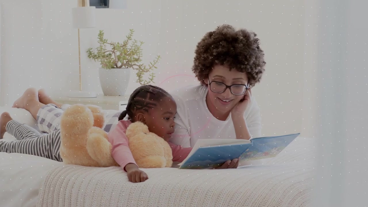 Adult woman and child lying on bed, turning picture book pages causing neon shapes for education