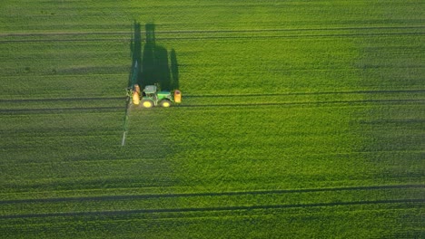 Aerial-establishing-view-of-a-farmer-spraying-crop-fields-with-tractor,-pesticide-and-fertilizer-spraying,-sunny-summer-evening,-golden-hour-light,-wide-birdseye-drone-dolly-shot-moving-right