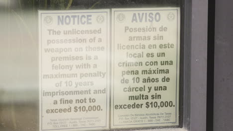 a gun warning notice in english and spanish on the front window of a store in dallas, texas