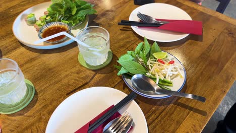 a sequence of preparing fresh vietnamese vegetable side dishes on a wooden table in a bangkok restaurant, with vibrant lighting
