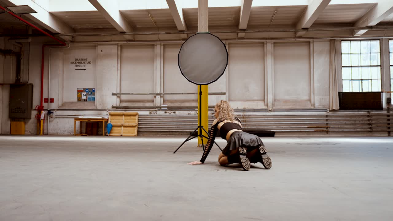 Young curly-haired woman posing on studio floor in edgy outfit