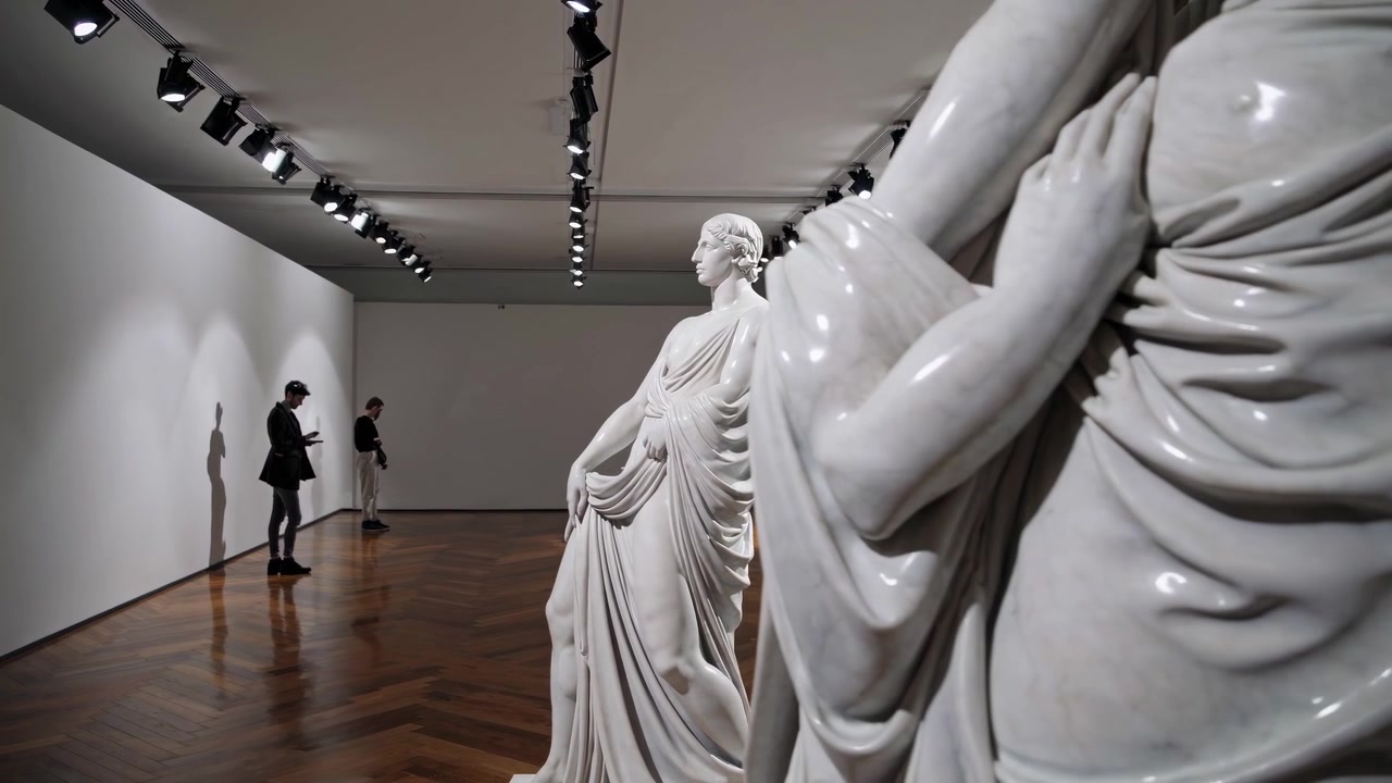 Visitatori che ammirano statue classiche in marmo in una galleria d'arte moderna.
