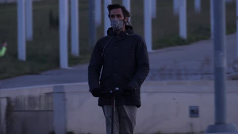 young man wearing face mask drives e scooter in urban park environment