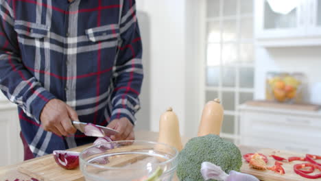 Midsection-of-senior-african-american-man-cooking,-chopping-onions-in-kitchen,-slow-motion