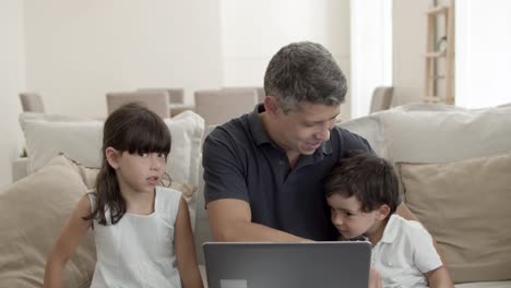 Papá-Alegre-Y-Dos-Niños-Lindos-Sentados-En-El-Sofá-Frente-A-La-Computadora-Portátil