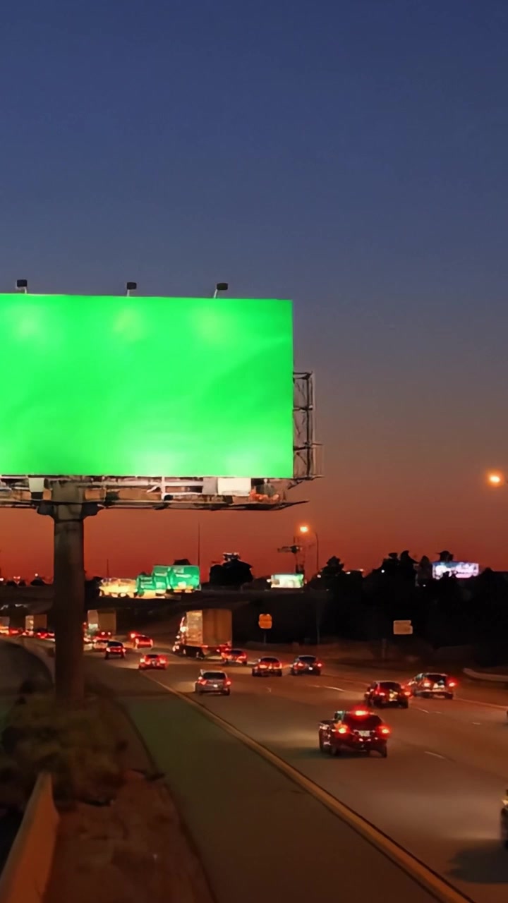 Vallas publicitarias iluminadas en la carretera al anochecer, haciendo la transición a la noche, mostrando vibrantes pantallas verdes sobre el tráfico denso que fluye por el bulevar de la ciudad
