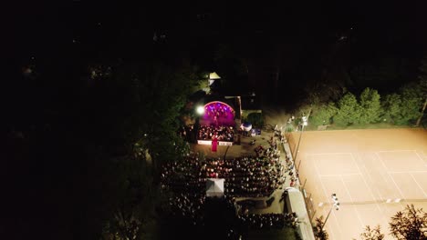 vista aérea de 4k de un concierto de música en vivo en un escenario iluminado en un parque público por la noche