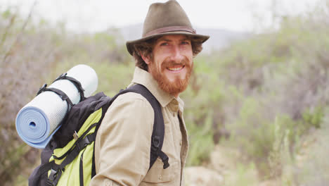 retrato de un sobreviviente caucásico barbudo sonriente caminando por el desierto con una mochila