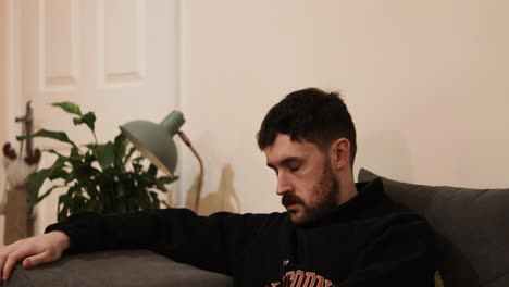 young man with facial hair falling to sleep while watching tv on the couch