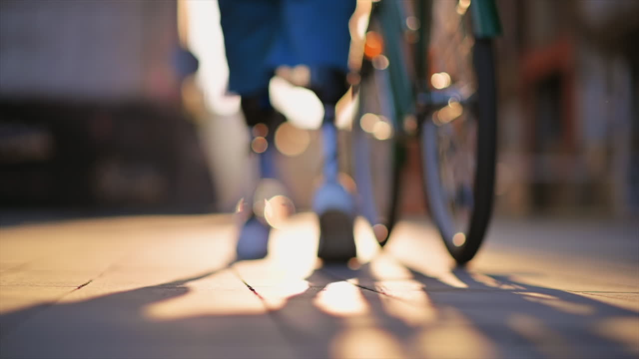 Slow motion view of a man with prosthetic legs. Walking with a bicycle on the street, sunset, out of focus effect
