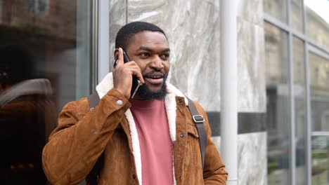 black man with shoulder backpack stands outdoor near the office center