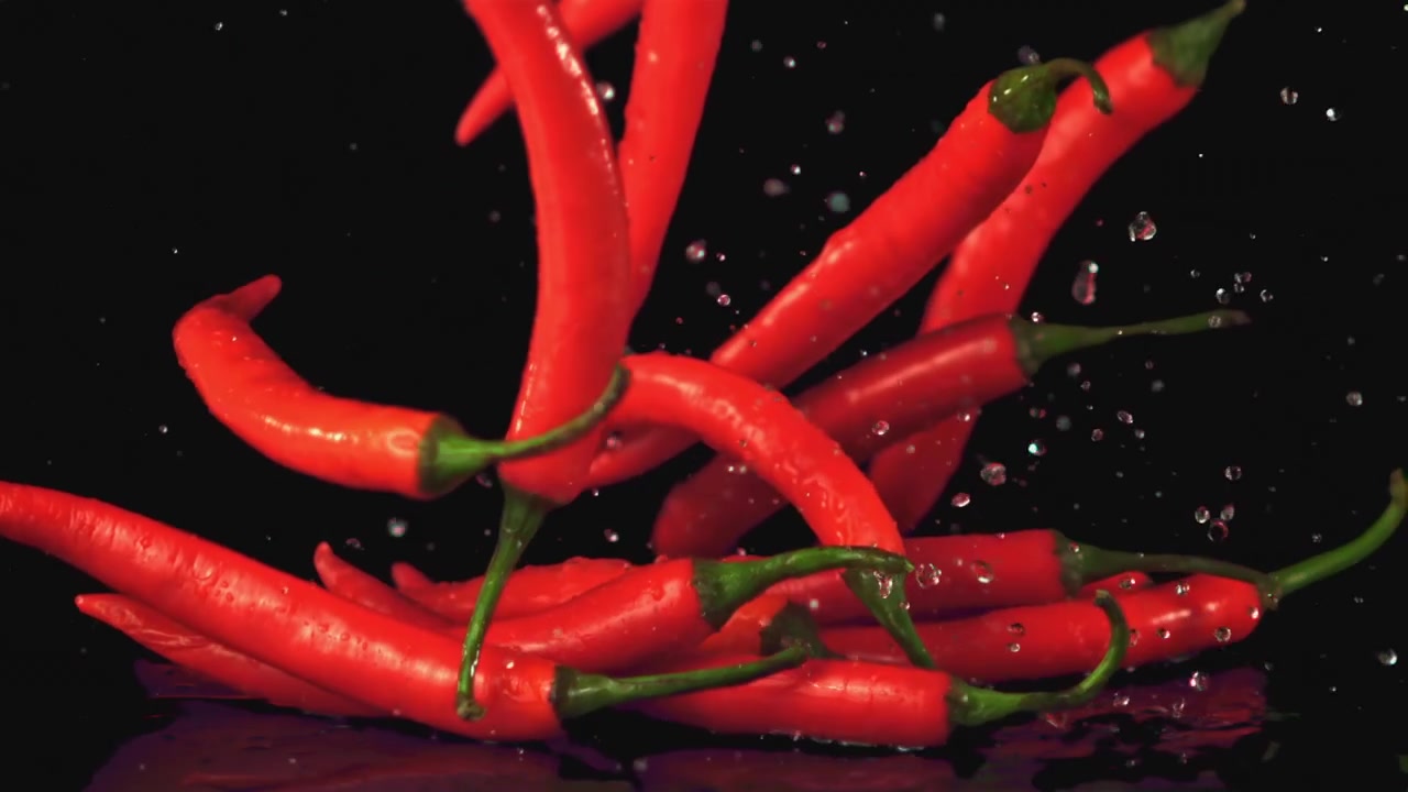 Red Chili Peppers Falling and Splashing on Wet Black Surface in Slow Motion