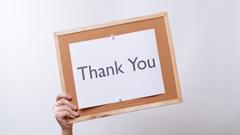 woman's hand shows the paper on board with the word thank you in white studio background with copy space