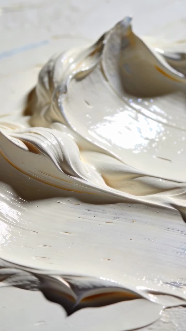 Video verticale: Crema beige che si muove reagendo allo spostamento della telecamera, depositandosi su una tavolozza, con segni di utensili.
