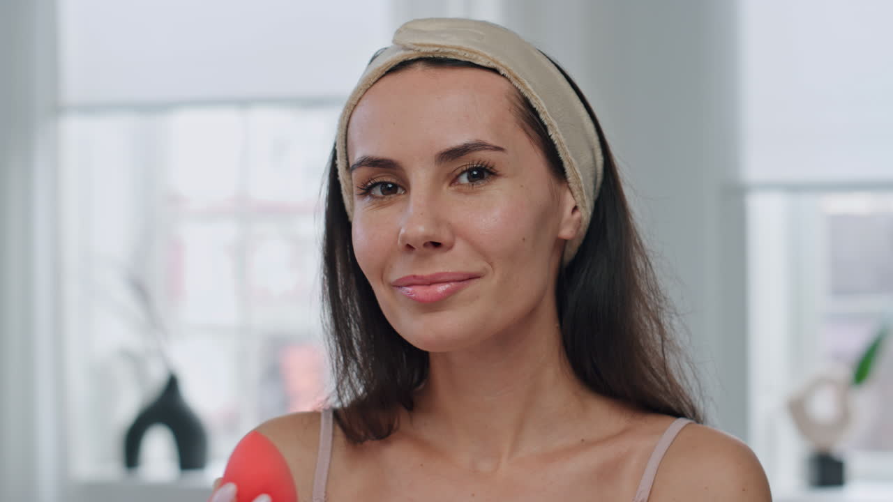 Donna sorridente che applica il fondotinta, ritratto POV allo specchio al chiuso. Donna con spugnetta per il trucco.