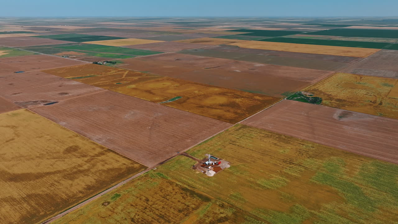 Vast field divided on rectangular pieces. A little site for oil production at one of the area. Aerial view.