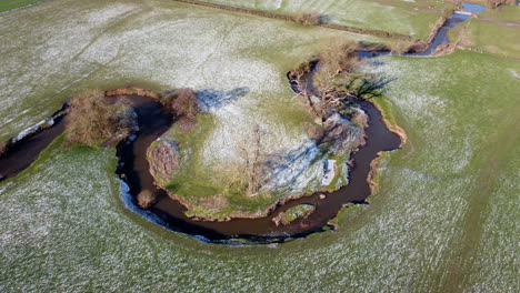 An-aerial-view-of-the-twisting-river-Arrow-running-through-fields-in-Warwickshire,-England-on-a-sunny-frosty-winter-morning