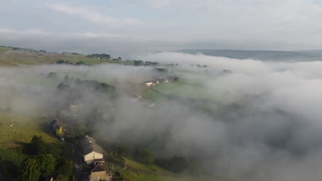 establishing shot, foggy morning over the yorkshire dales, meadow near a rural village, aerial view landscape moving through the clouds when it is sunny