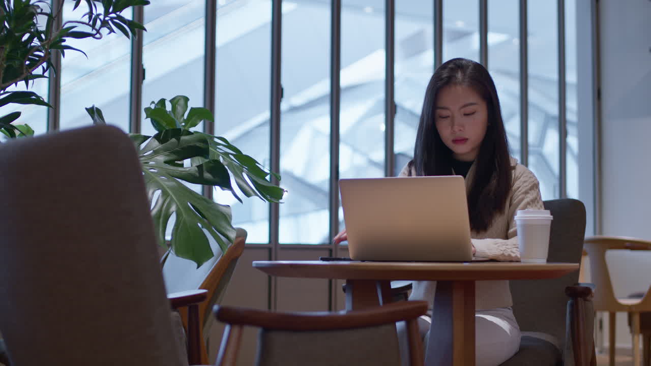 一位漂亮的亞洲女孩在咖啡店用手提電腦工作，同時查看手機訊息。