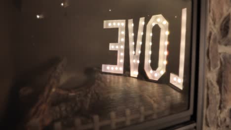 reflection off the glass of a fire place at a wedding reception of a giant lit up love letter sign