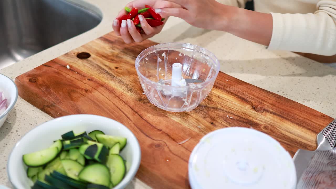 Hands using a manual food chopper to prepare vegetables on a wooden cutting board in a well-lit kitchen