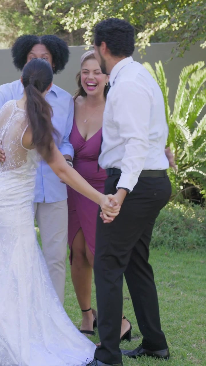 Video verticale: Amici si avvicinano per congratularsi e abbracciare gli sposi sul prato, con abito da sposa e cravatta.