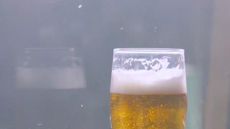 medium shot of drunk fresh cool lager beer in pint glass with bubbles rising in slow motion with glass background. alcohol beverage 4k.