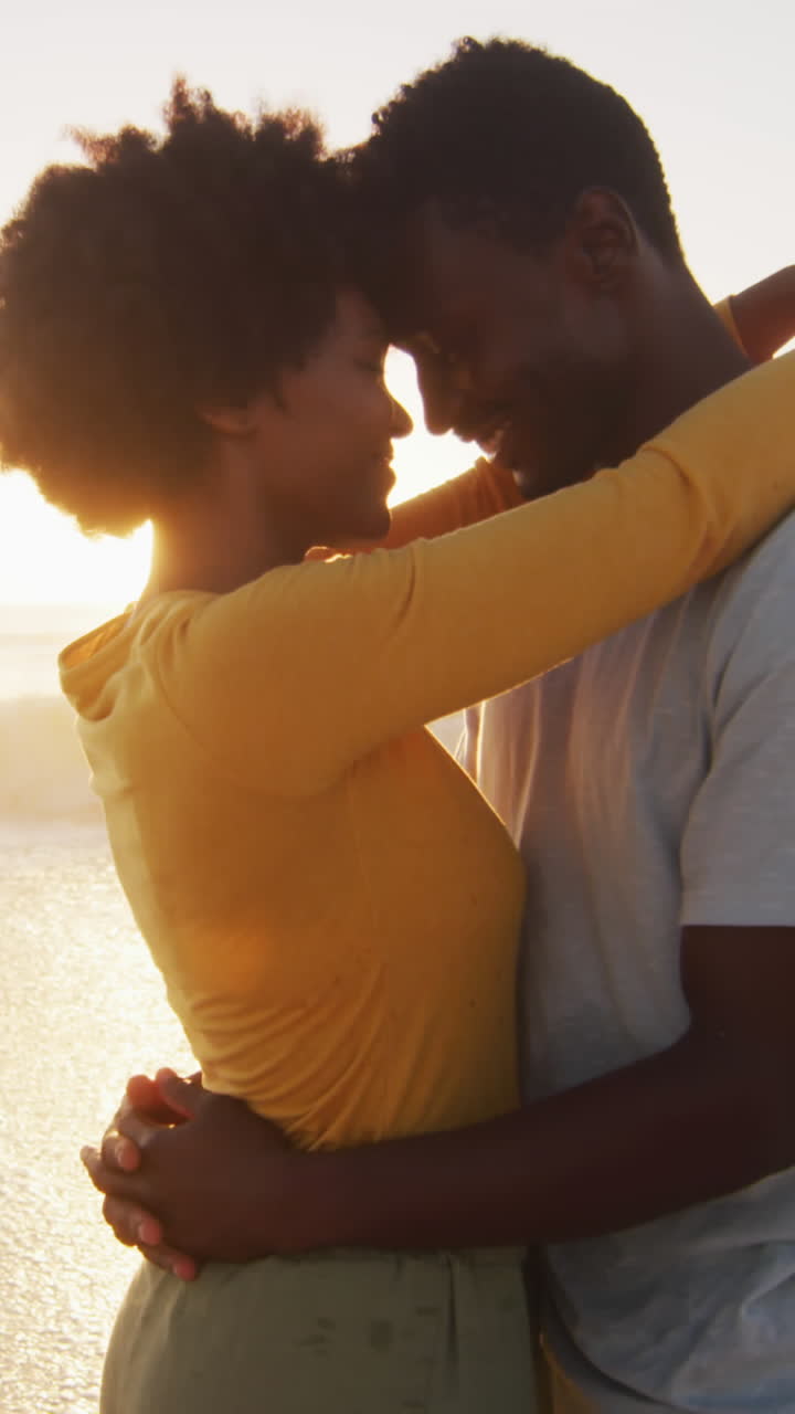 una pareja afroamericana sonriente abrazándose en el agua en una playa soleada