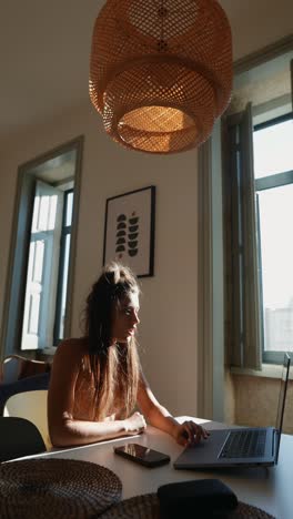 mujer trabajando en una computadora portátil en una oficina doméstica iluminada por el sol