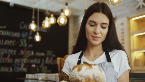 Cerca-De-La-Hermosa-Joven-Panadera-Mirando-La-Cámara-Mientras-Sostenía-Pan-Fresco-En-La-Tienda