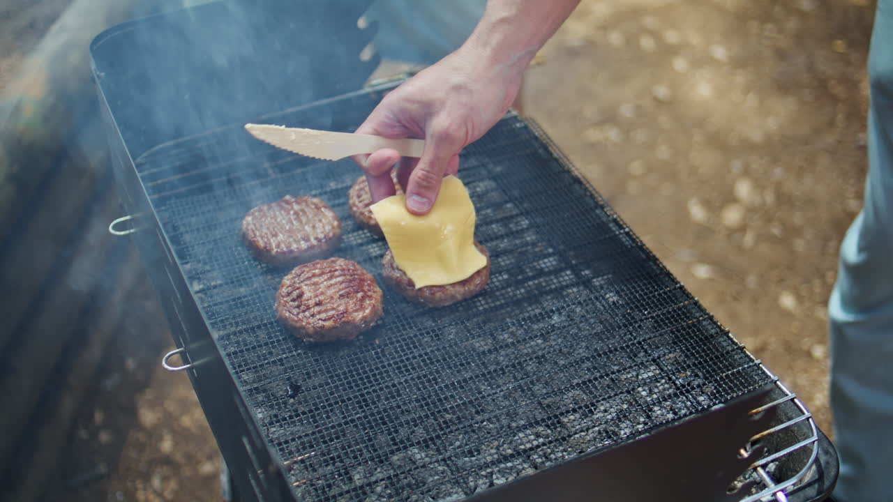 Man cooking bbq cheeseburger on smoky grill in sunny forest closeup. Unknown guy