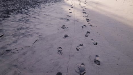 Drone-Volando-Cerca-Del-Suelo-Siguiendo-Algunos-Pasos-En-La-Arena-De-Una-Playa