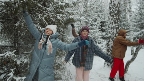 friends shaking snow off trees in winter forest