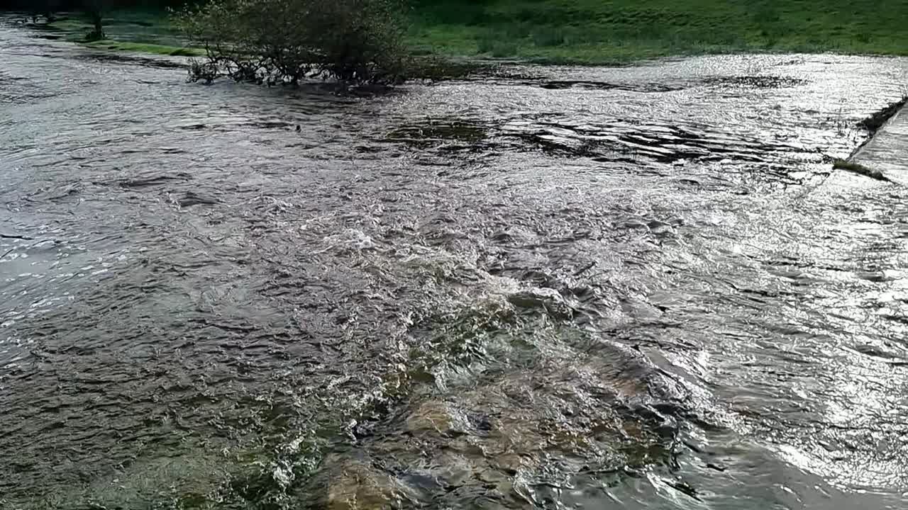 Slow motion devastated flooded countryside stream burst its banks with submerged trees after storm weather