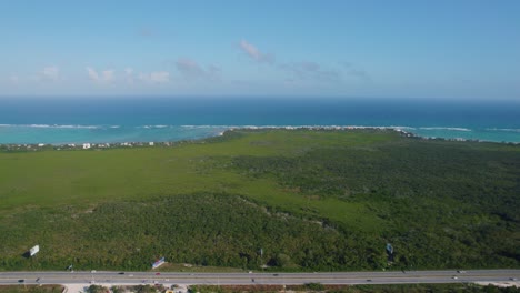 Toma-Aérea-En-Una-Extensión-Con-Vegetación-Verde-Y-Virgen-Con-Una-Carretera-Y-Al-Fondo-El-Horizonte-Con-El-Mar-Azul