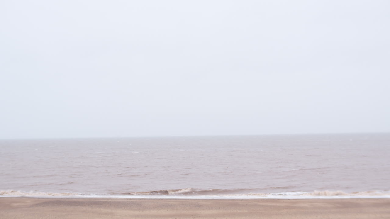 UK English Norfolk beach seaside with fog and mist over sea panning left across coast