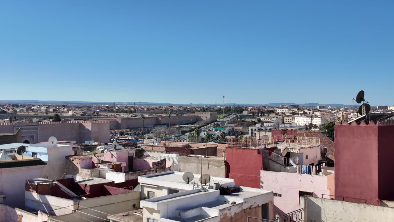 Wide cityscape of Meknes with red rooftops, towers and low rise buildings stretching outward establishing pan overview
