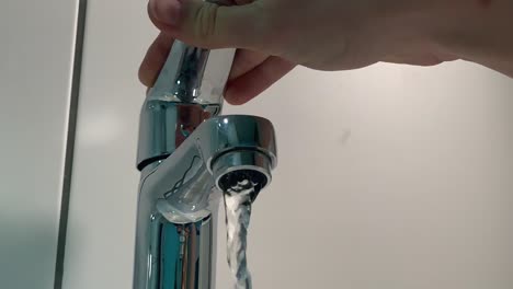 ultra slowmotion of opening the water tab in bathroom with white tiles in the background